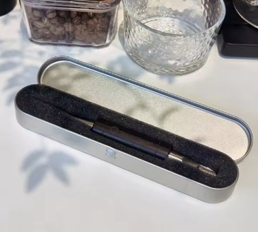 Black pen in a metallic case on a light surface with a glass and container in the background